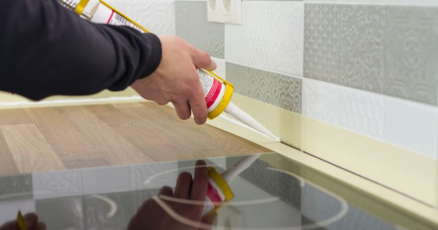 A person uses silicone to seal kitchen tiles. Thermosetting adhesives deform rather than melt if they are re-heated after curing, which makes them perfect for environments that involve exposure to high temperatures (like kitchens).