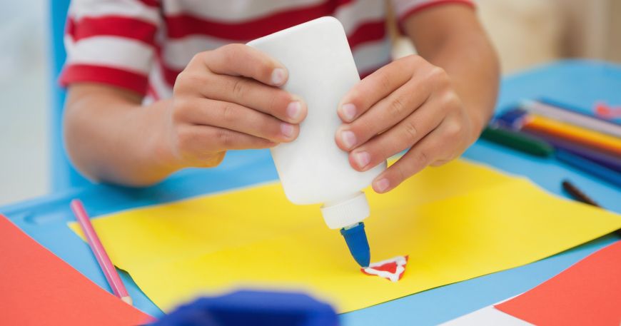 A child uses PVA glue to stick coloured paper together; PVA glue is a type of water soluble adhesive.