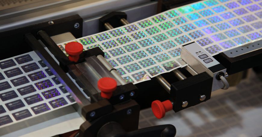 Holographic stickers being processed through a machine during production.
