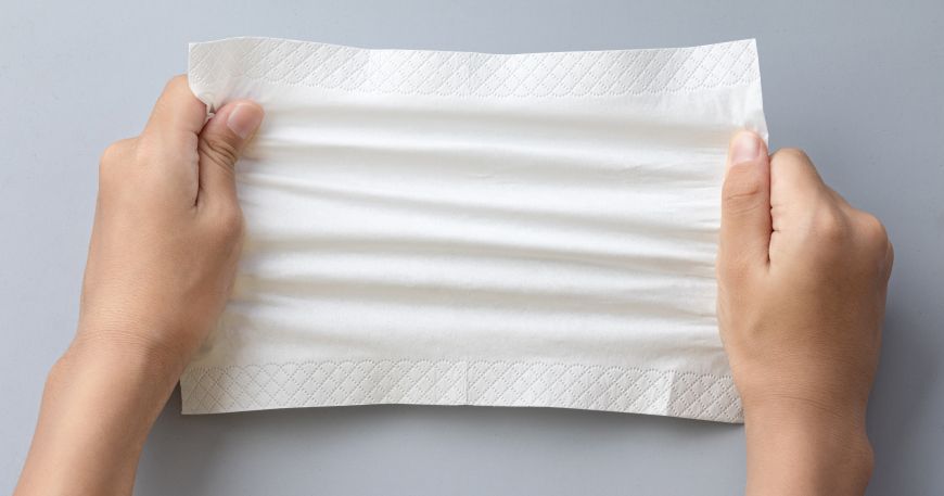 A paper napkin being pulled and stretched by a pair of hands; the tensile strength of the paper allows it to resist breaking (until the material's maximum tensile stress is applied).