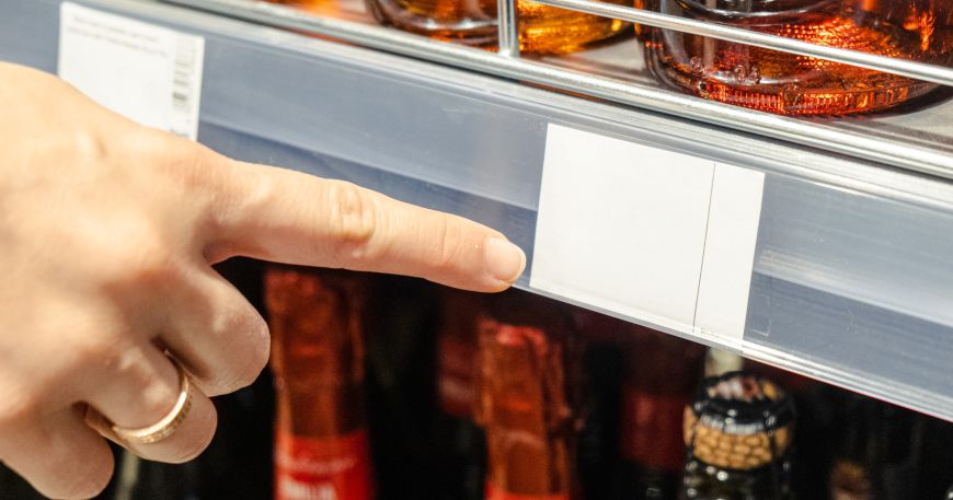 A person points to a shelf edge label. Fugitive adhesives hold these labels in place during manufacture and printing but are non-tacky once removed so labels can be slipped into shelf edge strips without sticking.