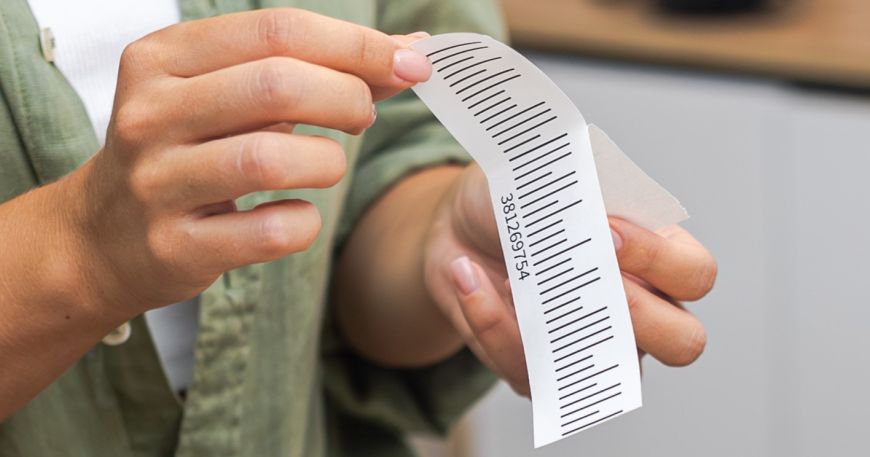 A person peels a label off its backing sheet; an anchor coat may be applied to the face material of a label to help it stick to adjacent layers (like the adhesive, coatings, or print).