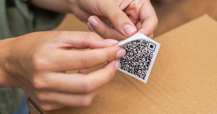 A person peeling a label off its backing sheet; a barrier coat may be applied to the underside of the face material of the label.