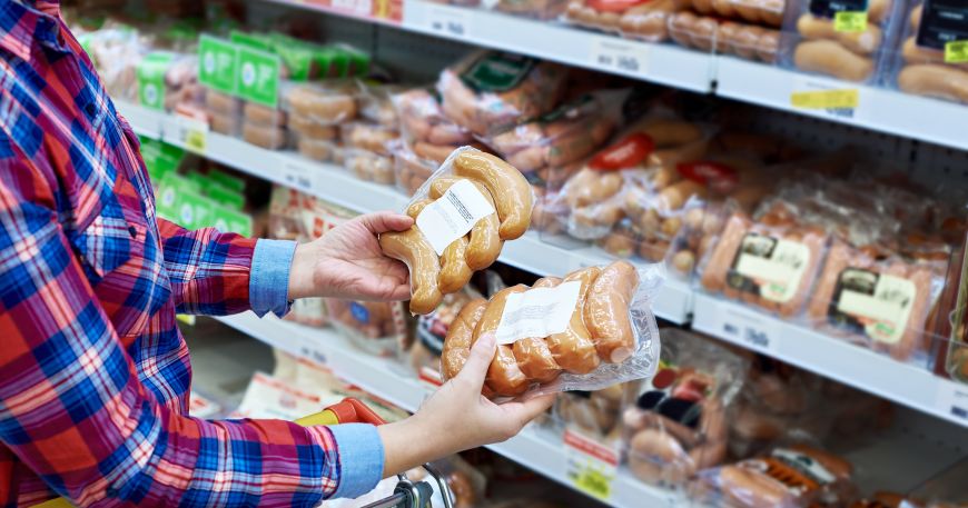 A person holding packages of sausages in a supermarket; the BgVV health and safety recommendations define what types of substances and materials (including those used to make labels) are suitable for food packaging.