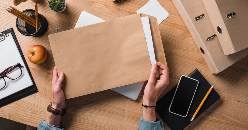 A person sat at an office desk holding a brown C4 envelope containing documents.